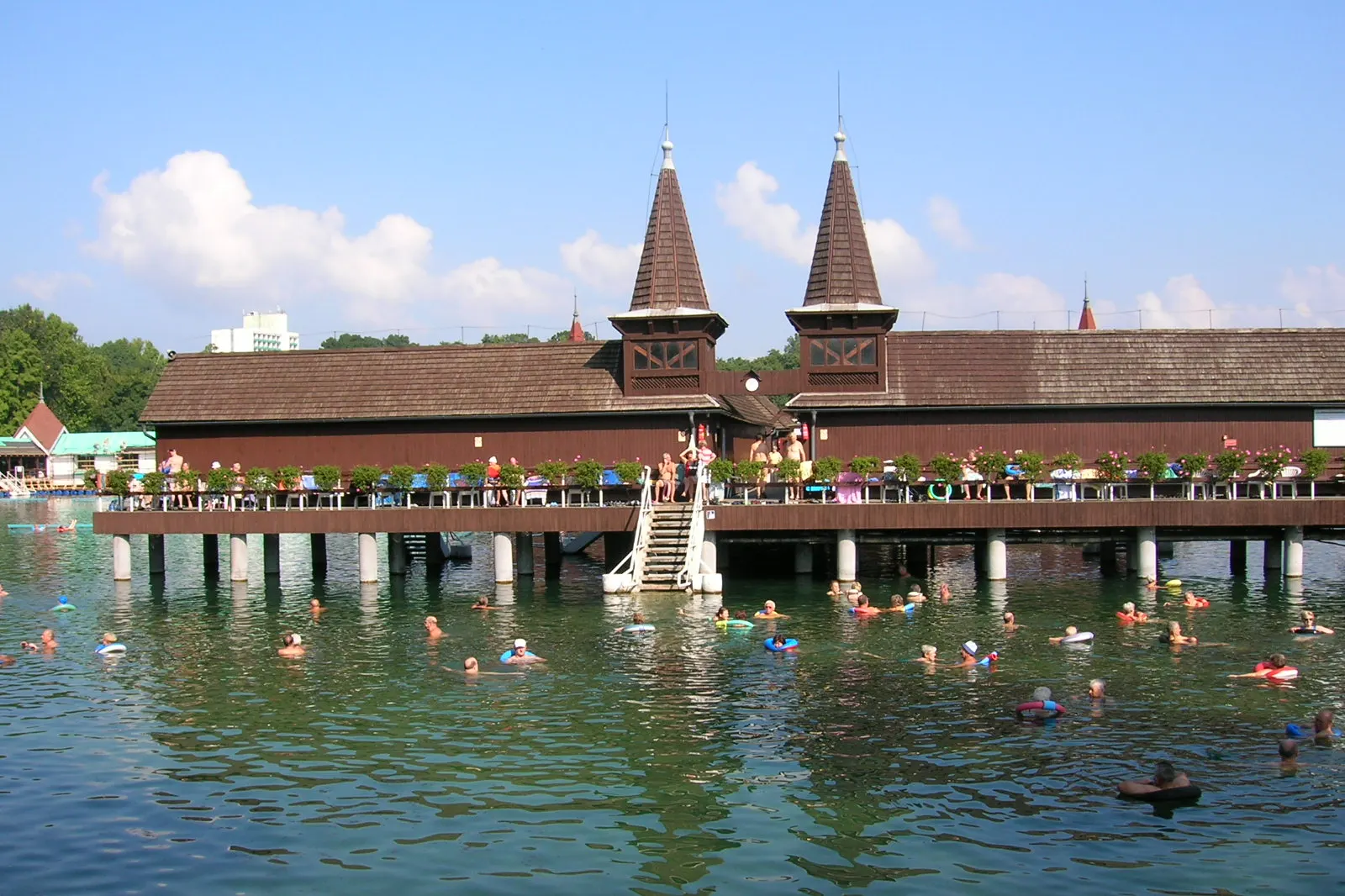 Vue d'ensemble du lac thermal de Hévíz avec le pavillon de baignade en bois et ses tourelles caractéristiques, baigneurs profitant de l'eau turquoise
